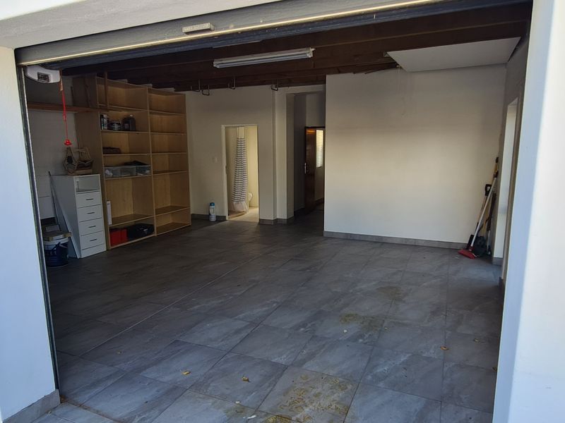 Spacious garage featuring tiled flooring, built-in shelving units, and exposed timber ceiling beams, offering versatile storage or parking space.