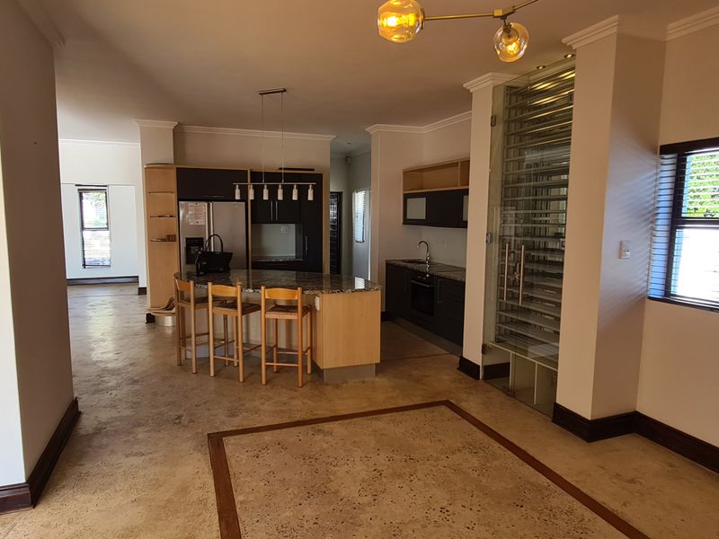 Spacious open-plan kitchen featuring a central island, stone countertops, integrated appliances, and a unique glass-fronted wine display, set against polished concrete flooring.