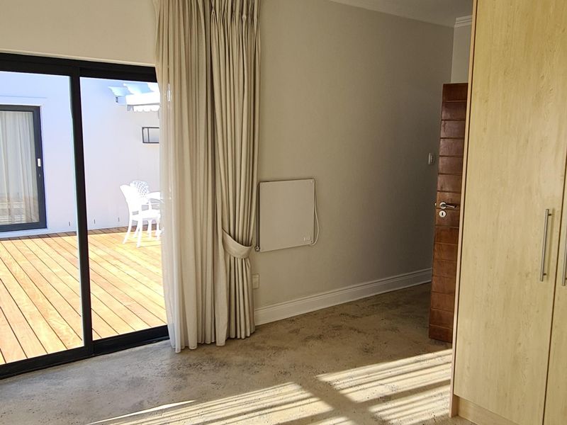 Bright bedroom featuring polished concrete floors, built-in wardrobe, and direct access to an outdoor wooden deck through sliding glass doors.