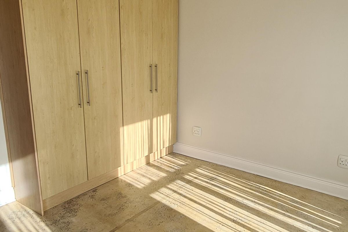 An empty bedroom featuring light wood-finish built-in cupboards and exposed concrete flooring, awaiting new floor finishes.