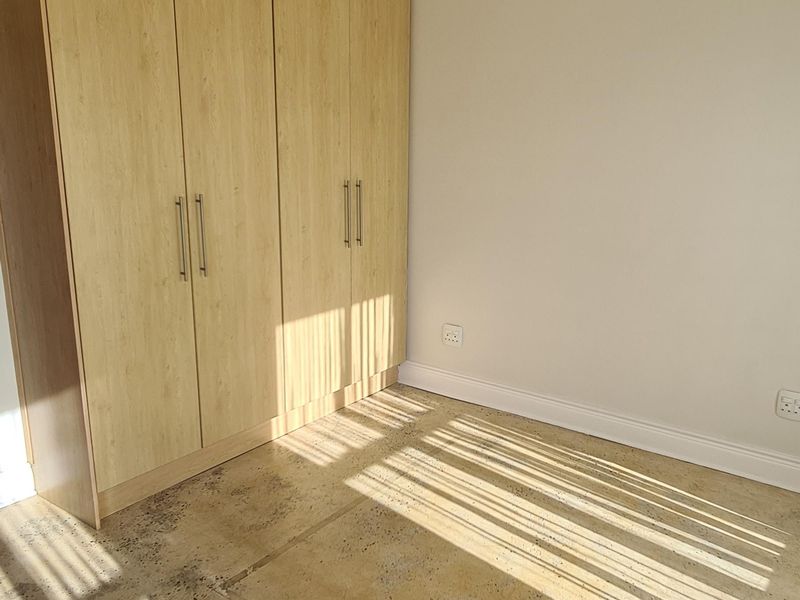 An empty bedroom featuring light wood-finish built-in cupboards and exposed concrete flooring, awaiting new floor finishes.