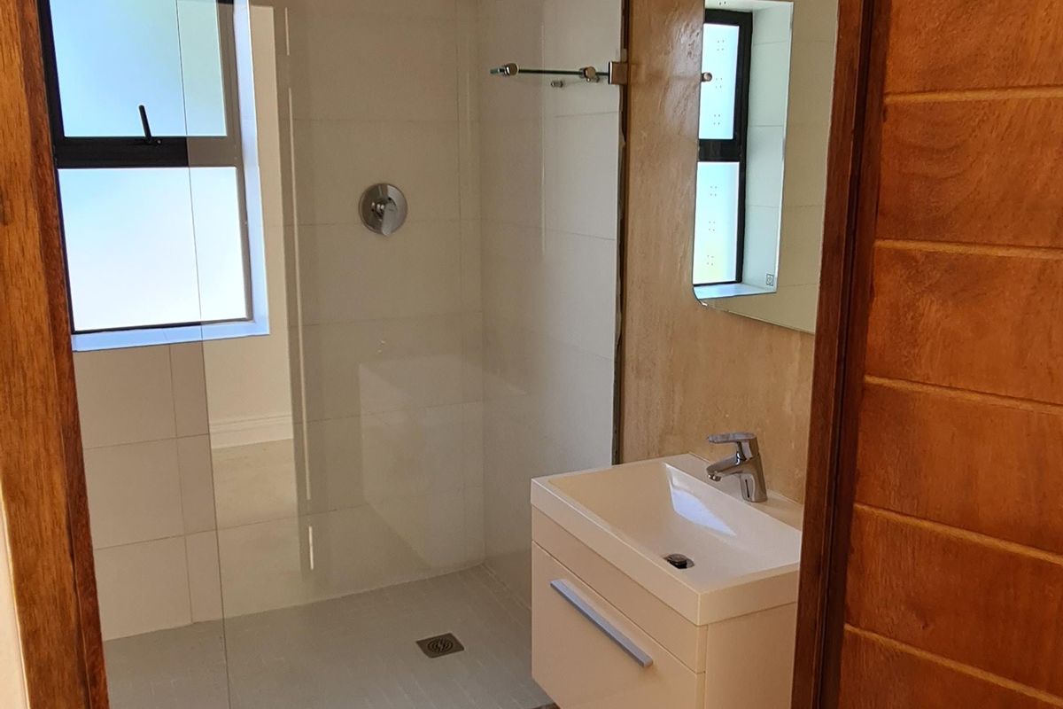 A compact bathroom featuring a glass-enclosed shower, wall-mounted vanity, and modern fixtures, currently requiring floor finishing.