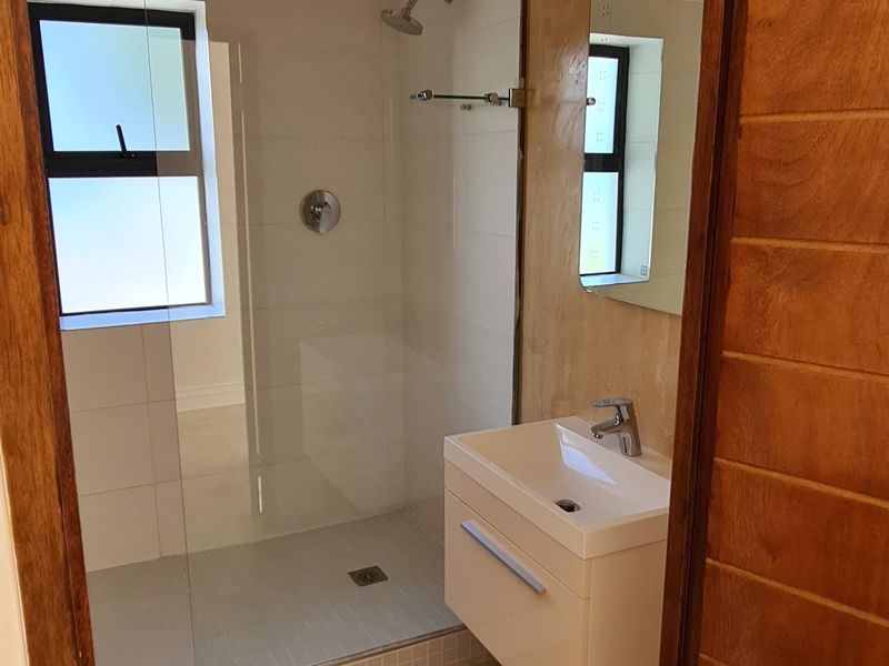 A compact bathroom featuring a glass-enclosed shower, wall-mounted vanity, and modern fixtures, currently requiring floor finishing.