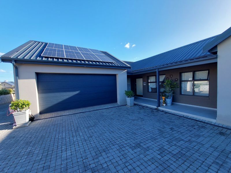 Front view of a modern home featuring a paved driveway, double garage, and roof-mounted solar panels under a clear blue sky.