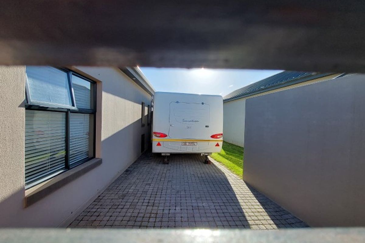 A side passage or rear exterior area featuring paved flooring, boundary walls, and top-hung windows.