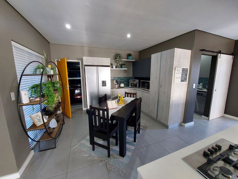 Modern open-plan kitchen and dining area featuring contemporary cabinetry, tiled flooring, and a functional layout with a convenient adjacent scullery access.