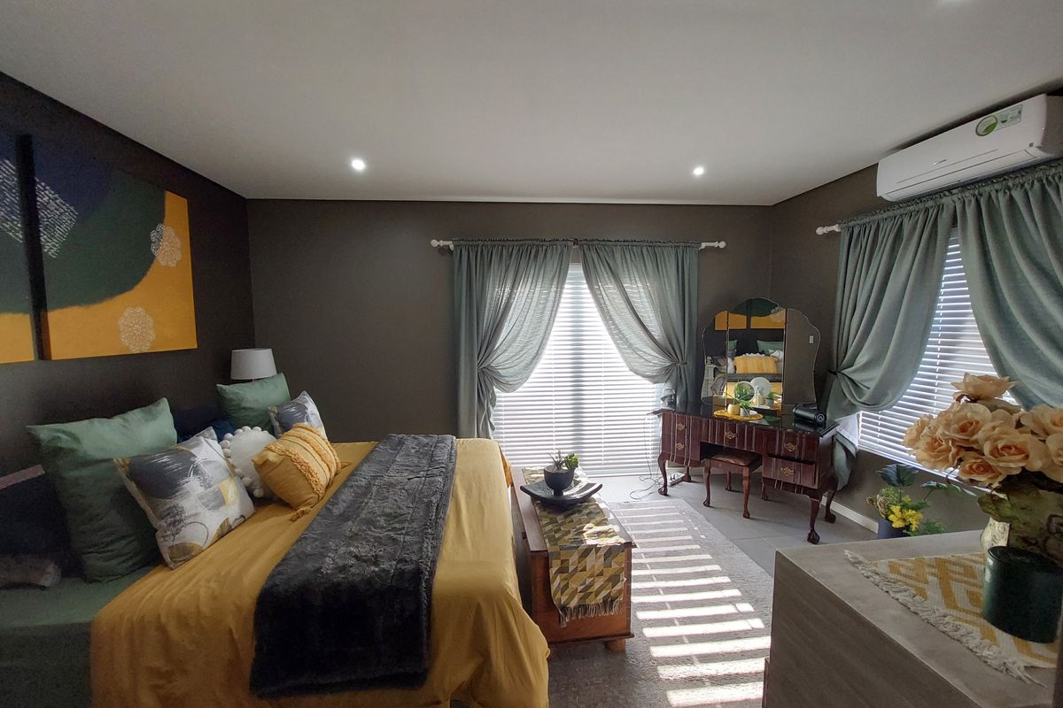 A well-maintained bedroom featuring recessed downlighting, a wall-mounted split-system air conditioner, and window treatments including venetian blinds and curtains.