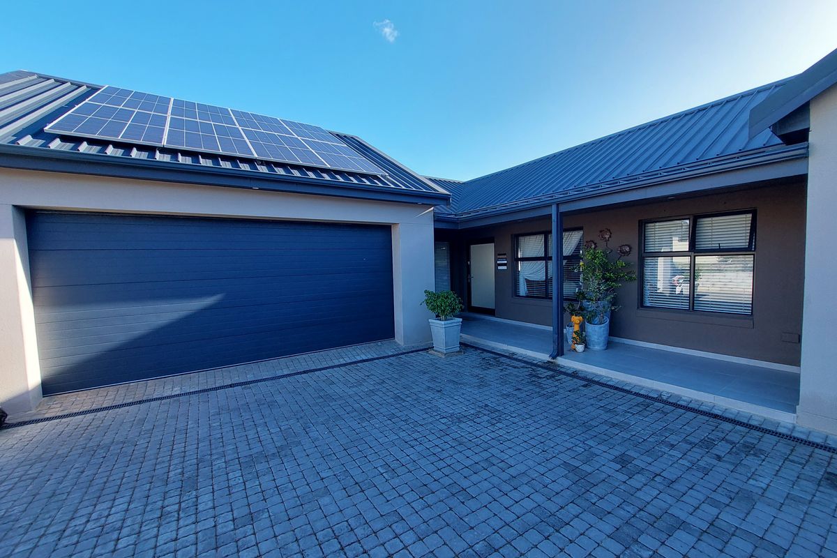Modern front elevation featuring a paved driveway, integrated garage, and roof-mounted solar panels, presenting a well-maintained and contemporary residential facade.