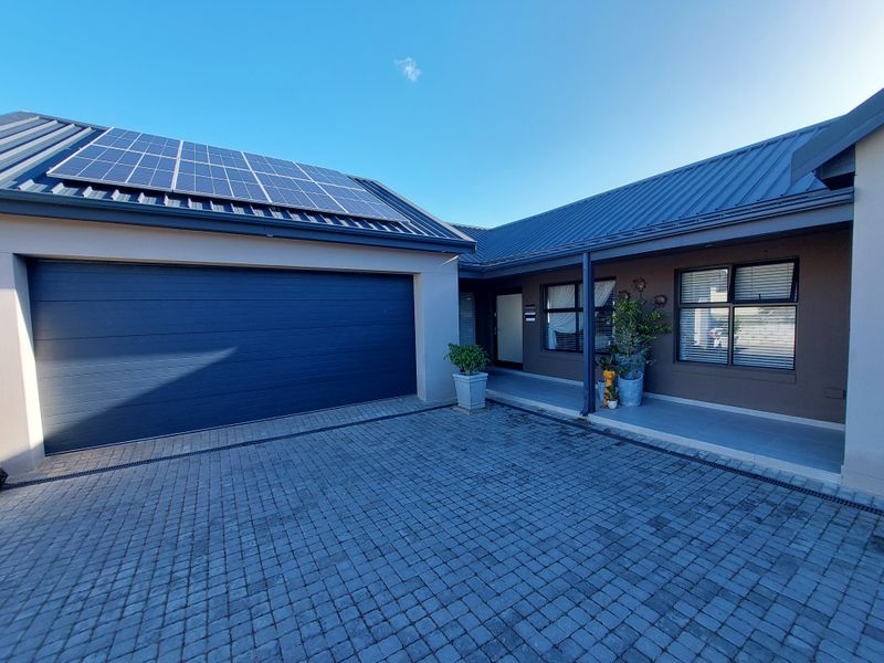 Modern front elevation featuring a paved driveway, integrated garage, and roof-mounted solar panels, presenting a well-maintained and contemporary residential facade.
