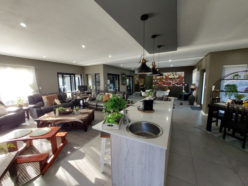 Spacious open-plan living area featuring a modern kitchen island with integrated hob and sink, recessed lighting, and large sliding doors leading outdoors.