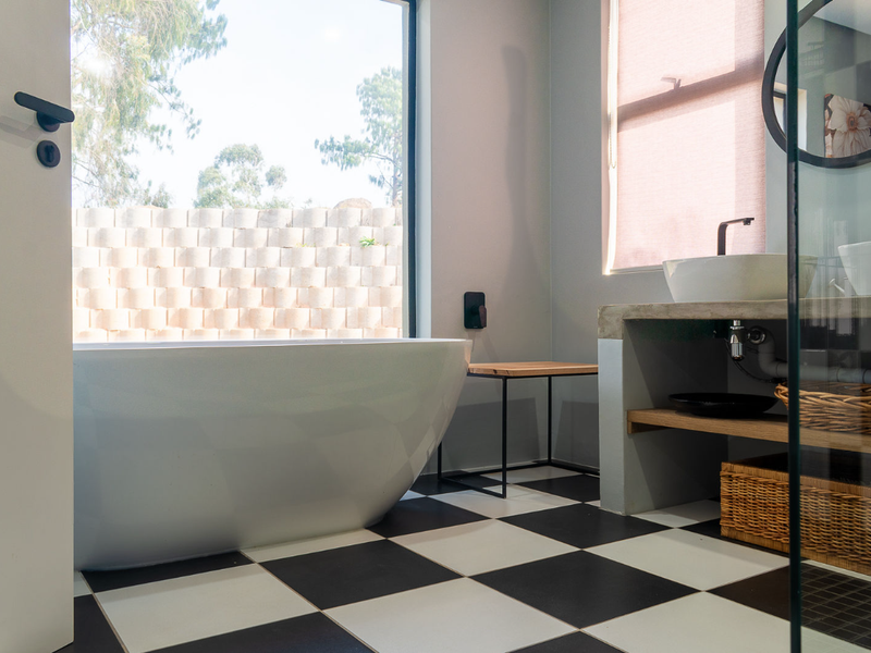 Modern bathroom featuring a freestanding bathtub, concrete vanity with vessel sink, black matte fixtures, and striking checkered floor tiles with large window views.