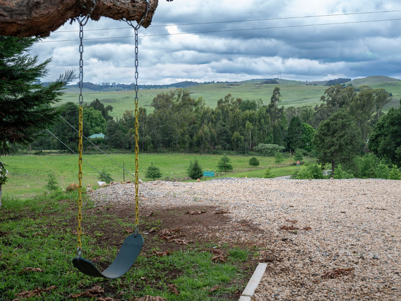 A scenic view overlooking a rural landscape with rolling hills, green fields, and a gravel driveway in the foreground.