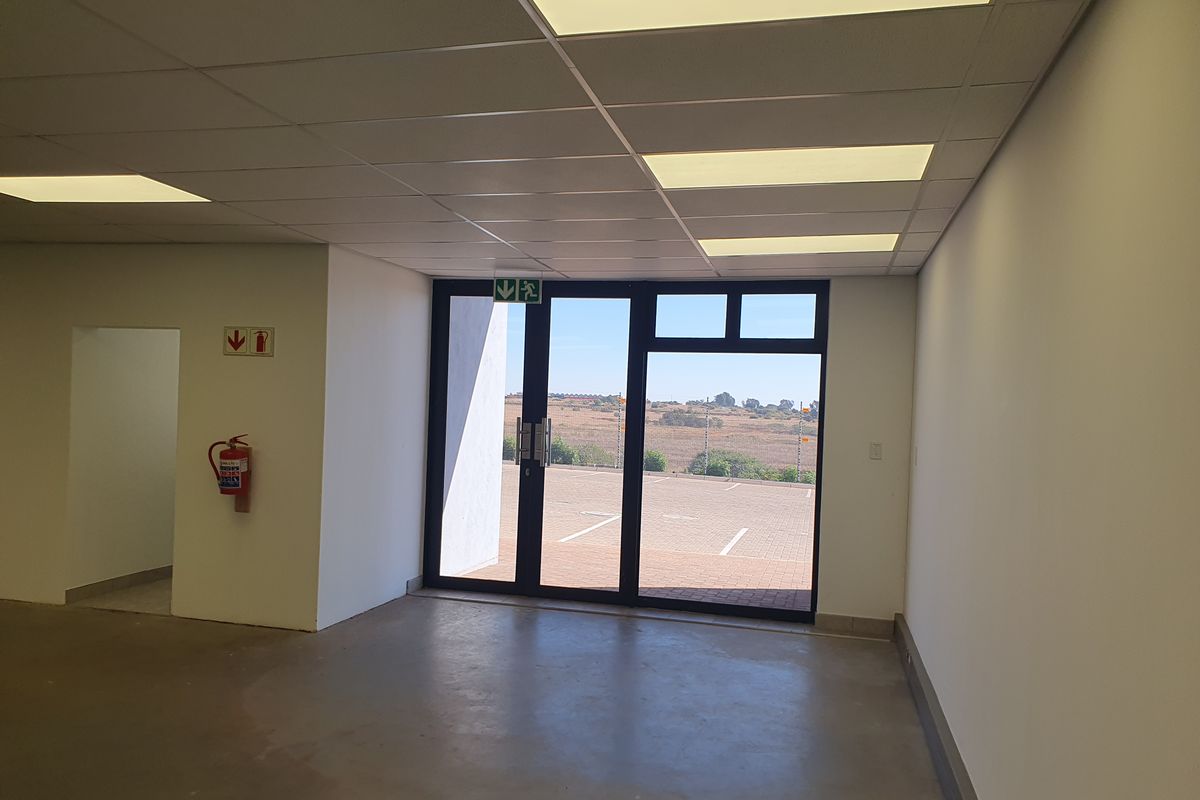 A clean, open-plan industrial entrance area featuring a suspended ceiling, recessed lighting, and a glass door leading to an exterior parking area.
