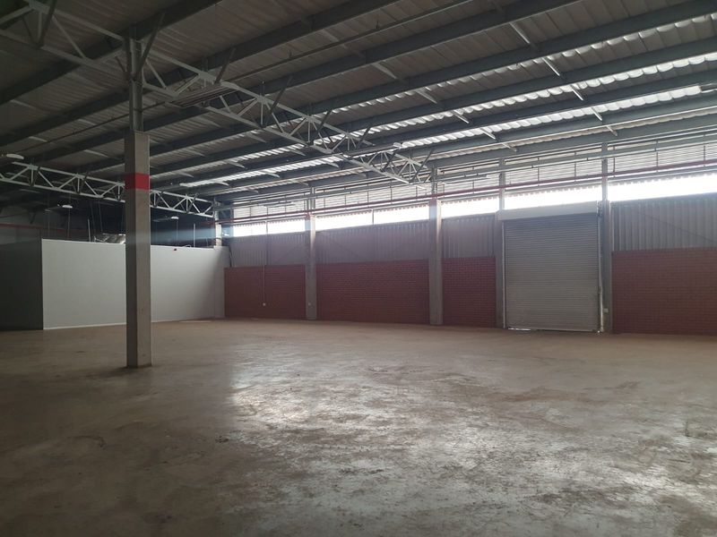 Spacious industrial warehouse unit featuring high exposed steel roof trusses, concrete flooring, and a large roller shutter door for easy access.
