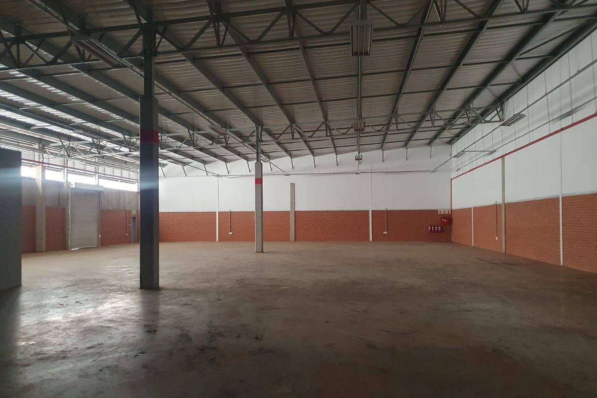 Spacious industrial warehouse featuring high ceilings with exposed steel trusses, concrete flooring, and a large roller shutter door for easy access.