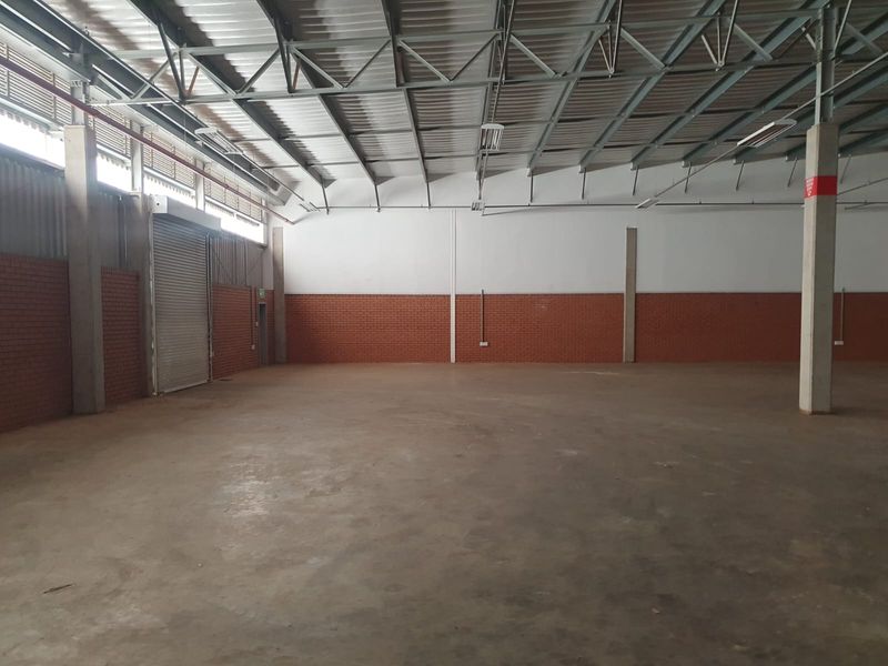 Spacious industrial warehouse unit featuring high ceilings with exposed steel trusses, concrete flooring, and a large roller shutter door for easy access.
