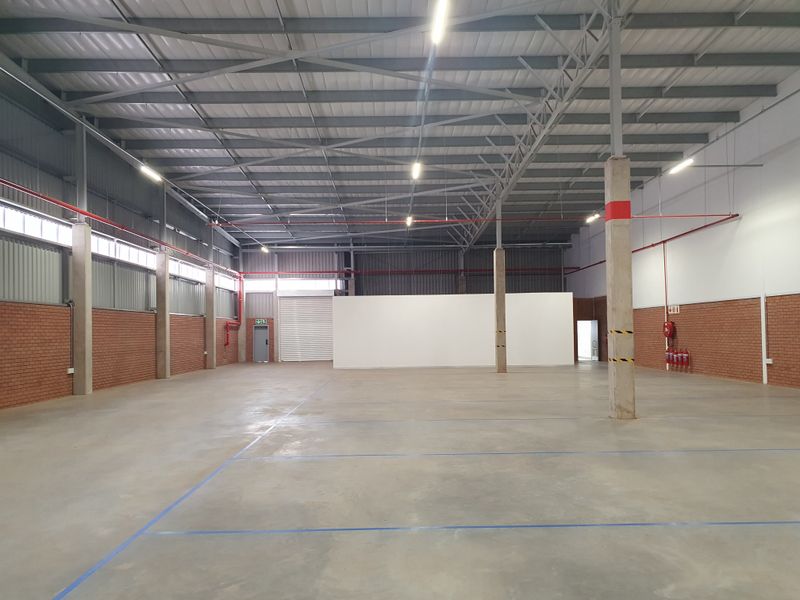 Spacious industrial warehouse unit featuring high ceilings with exposed steel trusses, concrete flooring, fire sprinkler system, and a roller shutter door.