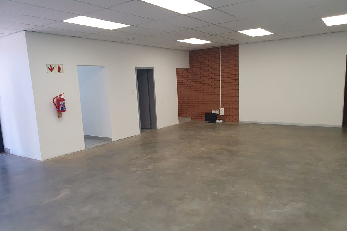 Spacious open-plan industrial office area featuring a suspended ceiling, recessed lighting, and an exposed brick feature wall with polished concrete flooring.