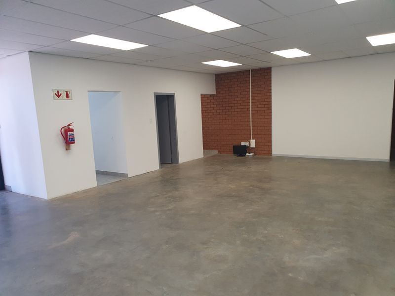 Spacious open-plan industrial office area featuring a suspended ceiling, recessed lighting, and an exposed brick feature wall with polished concrete flooring.