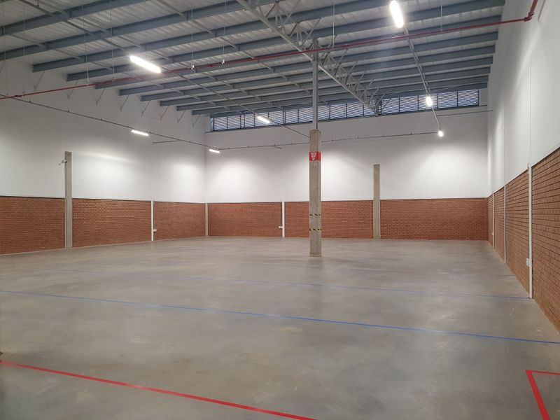 Spacious industrial warehouse unit featuring high ceilings with exposed steel trusses, concrete flooring, brick wall finishes, and integrated fire sprinkler systems.