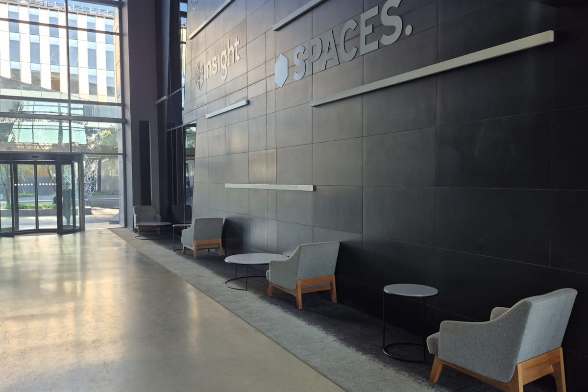 Modern office building entrance lobby featuring polished concrete floors, a striking dark feature wall, and expansive floor-to-ceiling glass windows.