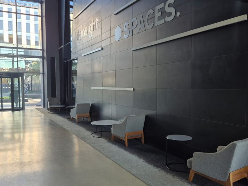 Modern office building entrance lobby featuring polished concrete floors, a striking dark feature wall, and expansive floor-to-ceiling glass windows.