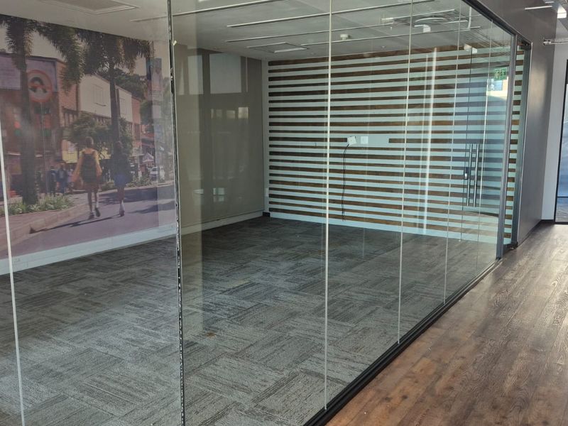 A modern, vacant office space featuring glass partition walls, a decorative slatted wood accent wall, and a combination of carpet and wood laminate flooring.