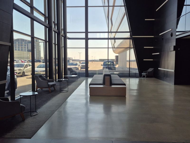 Modern office building entrance lobby featuring expansive floor-to-ceiling glass windows, polished concrete floors, and contemporary architectural wall finishes.
