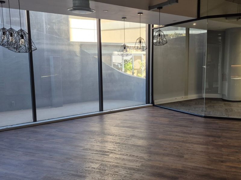 A modern, empty office space featuring floor-to-ceiling glass partitions, laminate wood flooring, and contemporary pendant lighting, offering a clean and professional work environment.