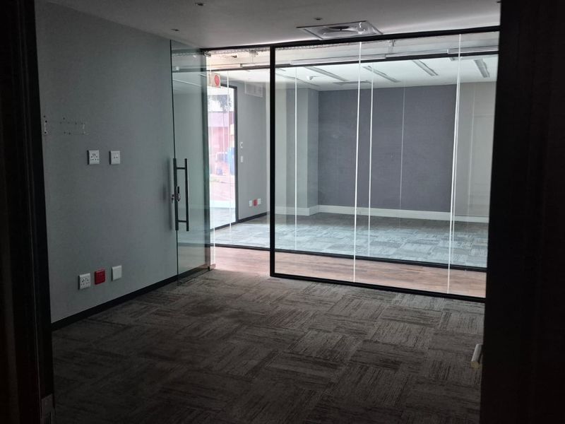 A modern, empty office space featuring glass partitions, carpeted flooring, and recessed ceiling lighting, providing a clean and professional environment.