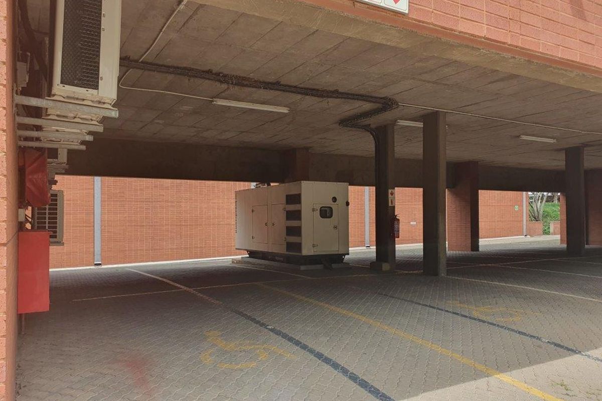 Covered parking area featuring a brick facade, concrete ceiling, and a dedicated backup generator unit.