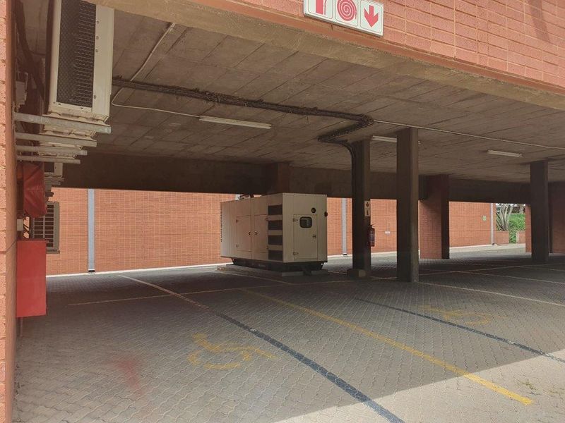 Covered parking area featuring a brick facade, concrete ceiling, and a dedicated backup generator unit.