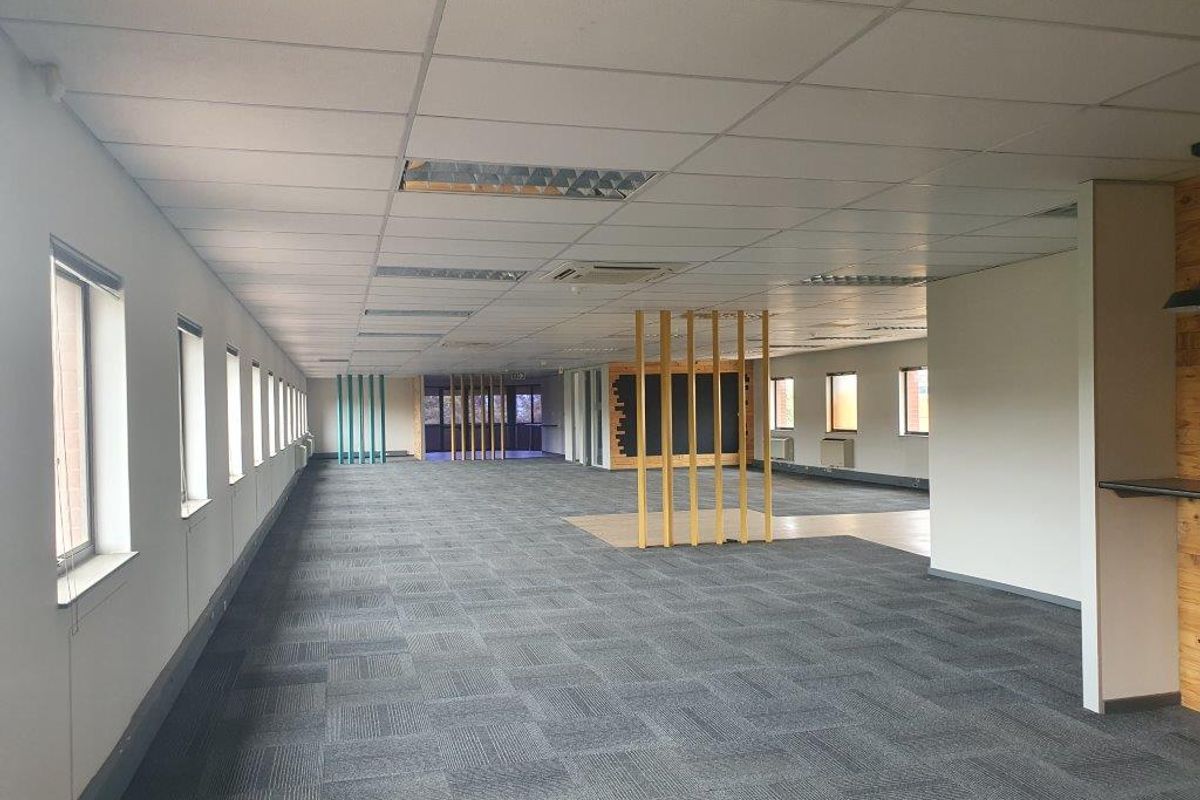 A spacious, open-plan office area featuring carpet tiles, a suspended ceiling with recessed lighting, and decorative timber slat room dividers.