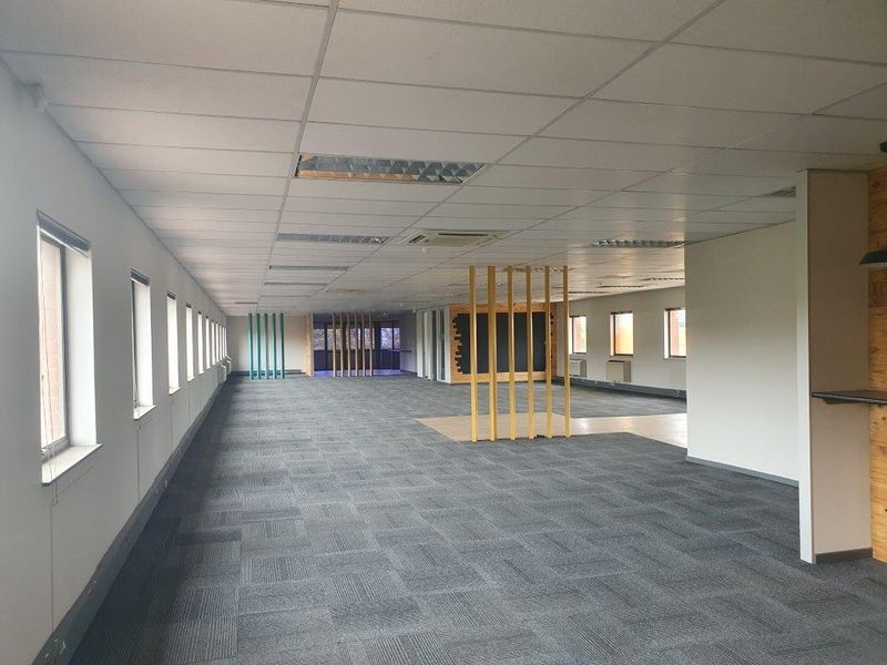 A spacious, open-plan office area featuring carpet tiles, a suspended ceiling with recessed lighting, and decorative timber slat room dividers.