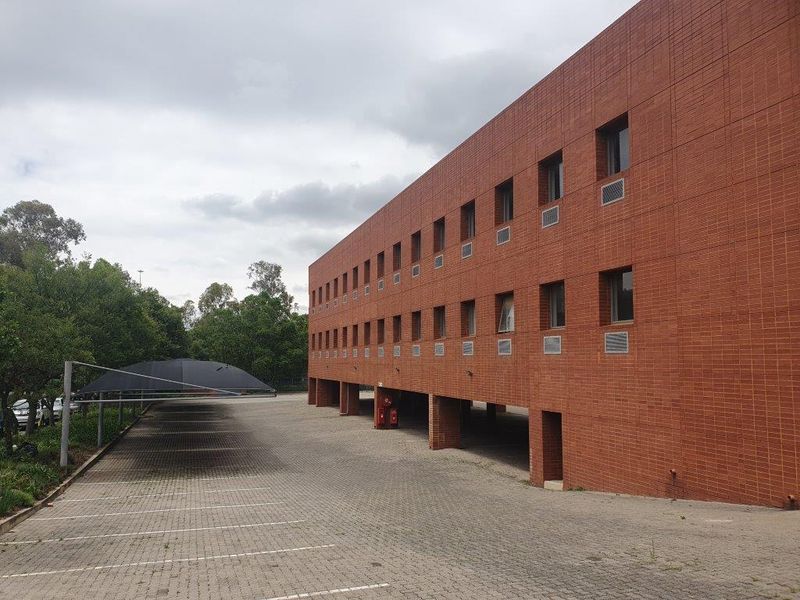 Exterior view of a multi-story brick office building featuring a large paved parking area with shade cloth carports.