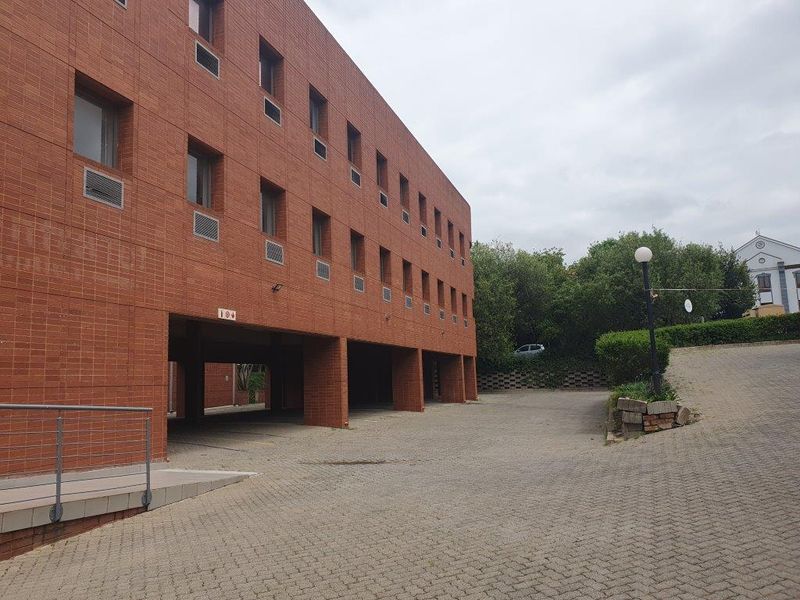 Exterior view of a multi-story brick office building featuring an undercover parking area and a paved driveway approach.