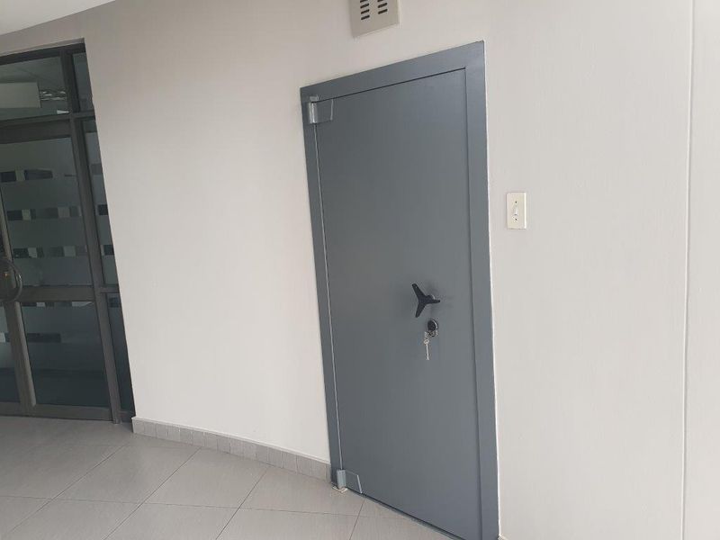 A clean office hallway featuring a secure metal door, tiled flooring, and neutral wall finishes.