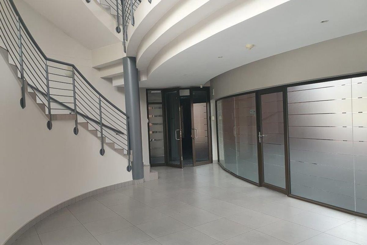 Spacious office entrance foyer featuring a curved staircase, tiled flooring, and modern glass partition walls, providing a professional and welcoming reception area.