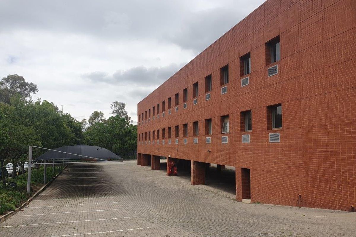 Exterior view of a multi-story brick office building featuring a large paved parking area with shade cloth carports.