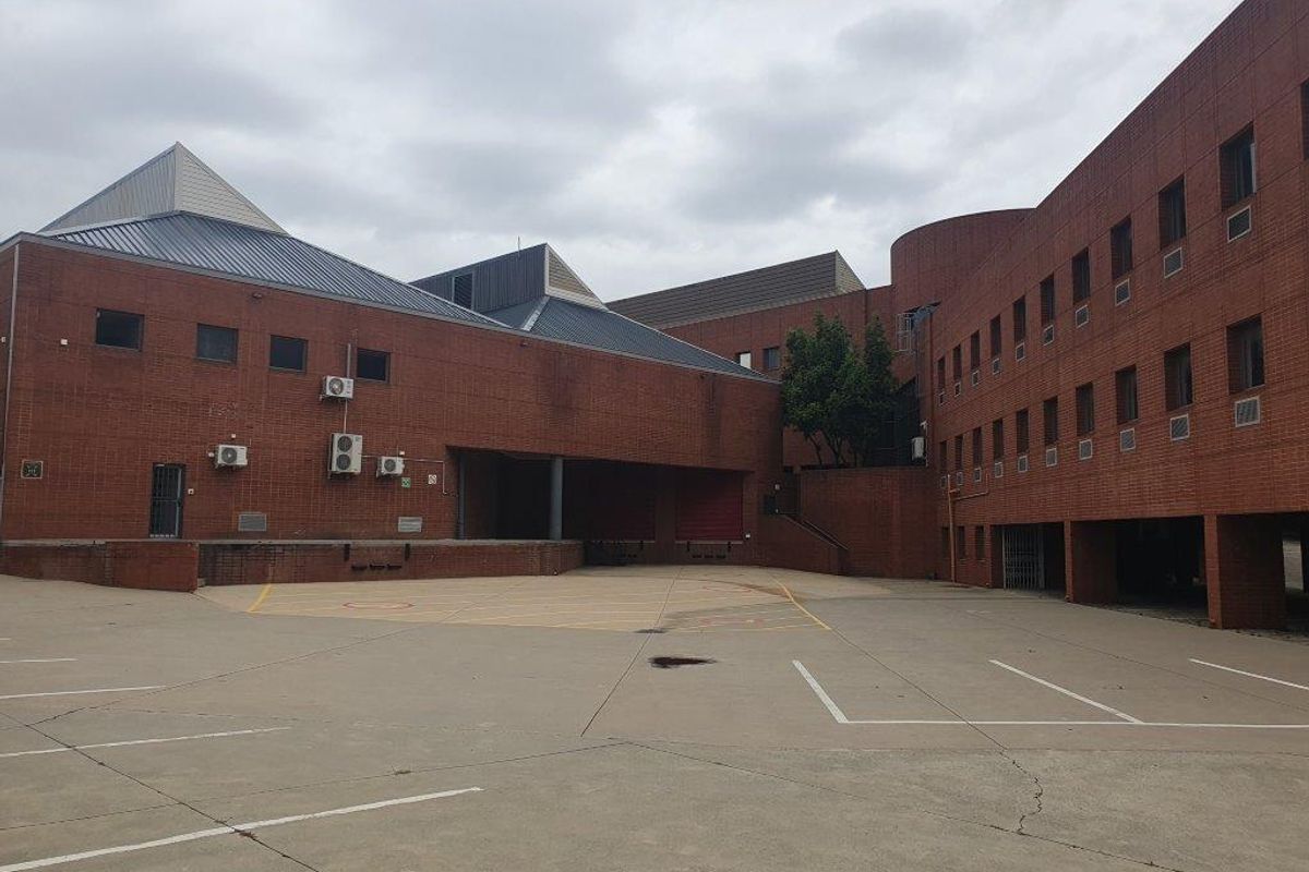 Rear exterior view of a large brick office complex featuring a loading dock area, concrete yard, and multiple external air conditioning units.