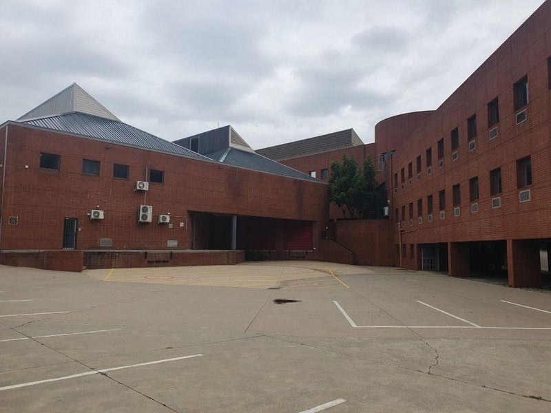Rear exterior view of a large brick office complex featuring a loading dock area, concrete yard, and multiple external air conditioning units.
