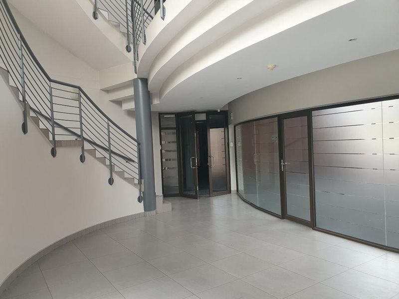 Spacious office entrance foyer featuring a curved staircase, tiled flooring, and modern glass partition walls, providing a professional and welcoming reception area.