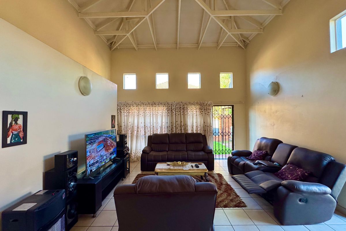 Spacious living room featuring a high vaulted ceiling with exposed trusses, tiled flooring, and direct access to the exterior through a security gate.