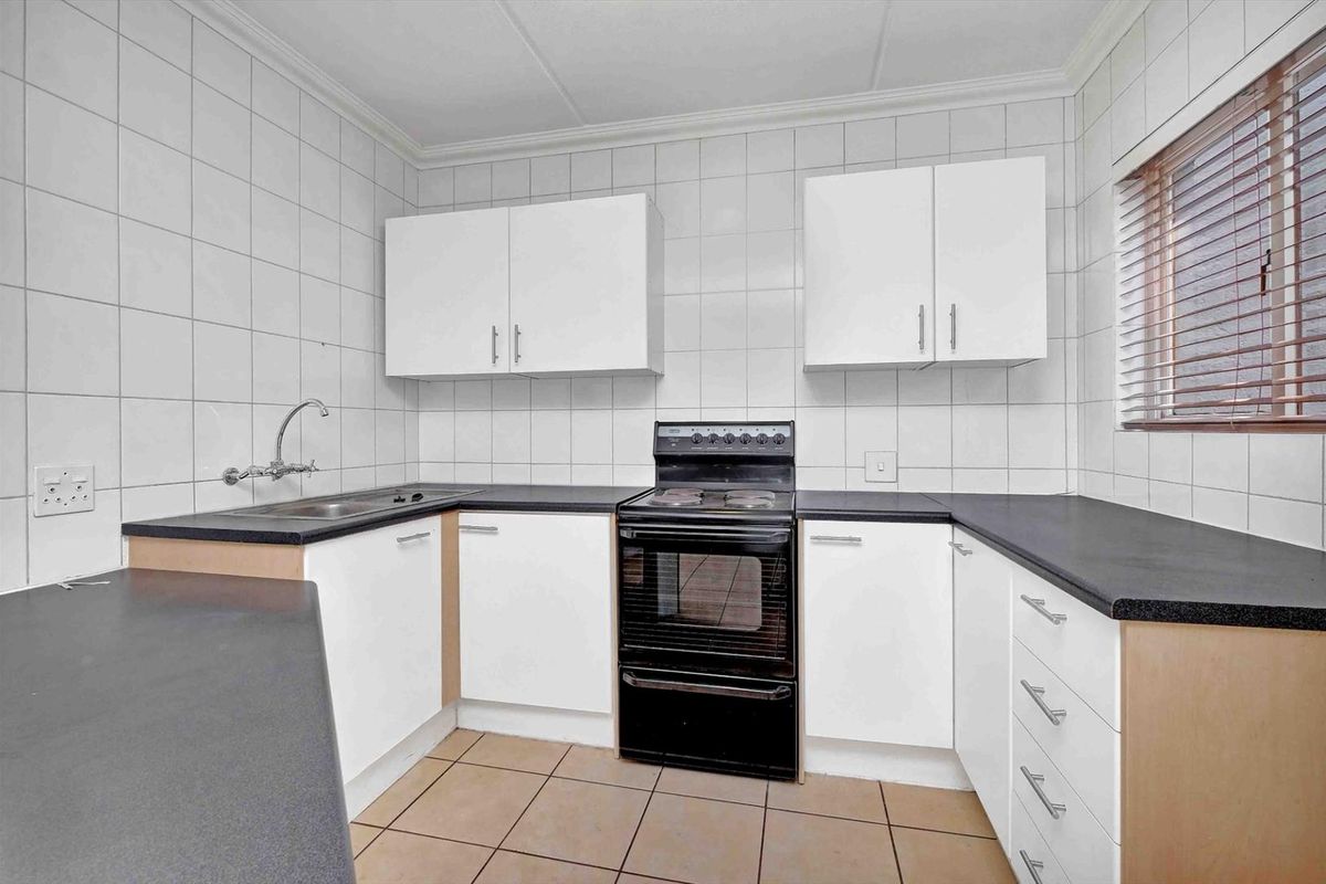 A functional kitchen featuring white cabinetry, dark countertops, tiled walls, and a freestanding electric stove.
