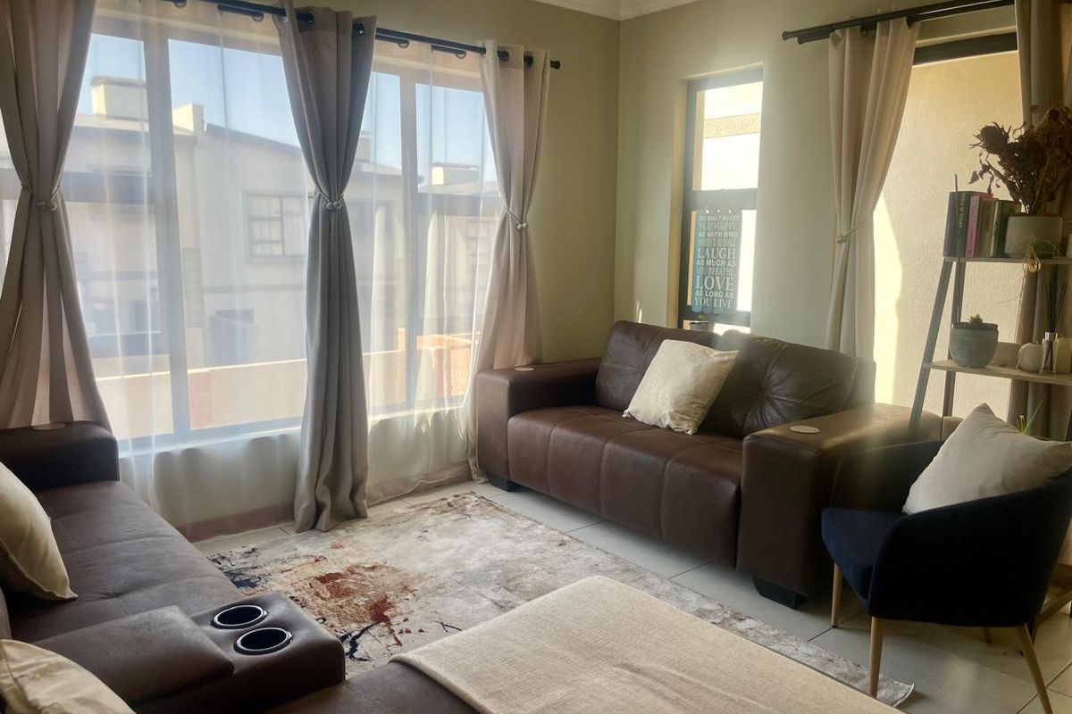 A bright living room featuring large windows with natural light, tiled flooring, and neutral wall finishes.