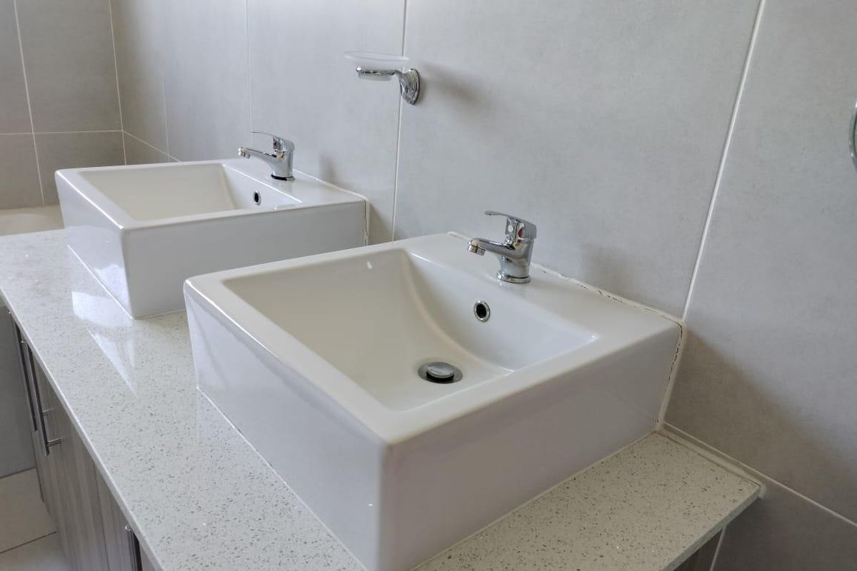 A modern bathroom vanity featuring dual square vessel sinks, chrome faucets, and a speckled stone countertop with neutral wall tiling.