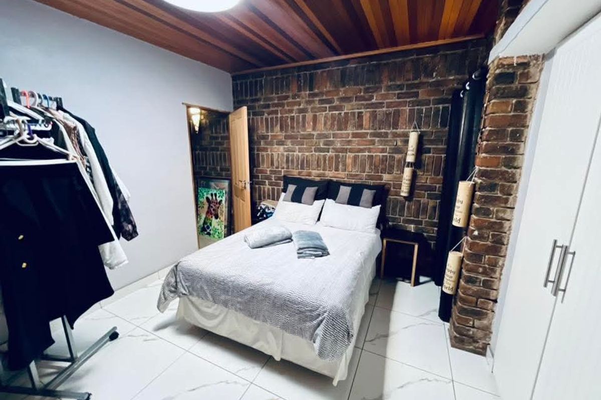 Bedroom featuring an exposed brick feature wall, timber ceiling, tiled flooring, and built-in wardrobe storage.