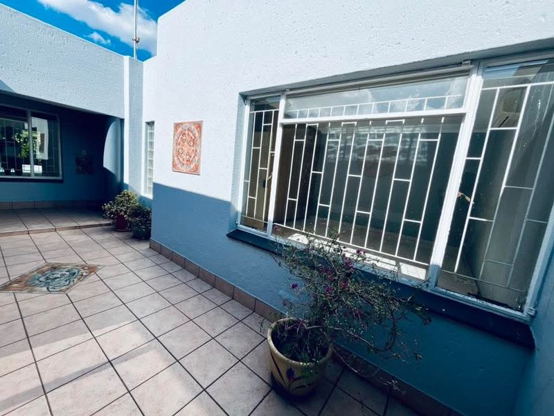 A covered patio area featuring tiled flooring and large windows with security bars, providing a functional outdoor space.