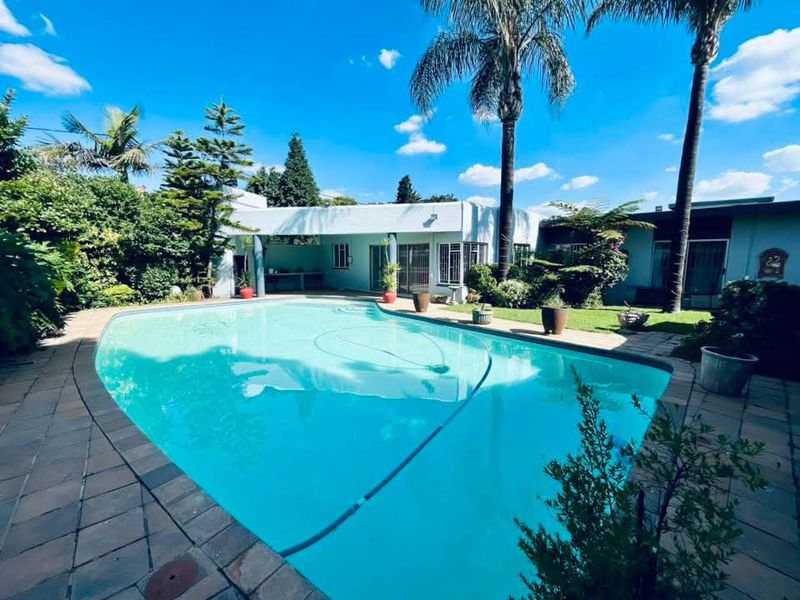 A well-maintained swimming pool area featuring a paved deck, established garden, and a covered patio space ideal for outdoor relaxation.