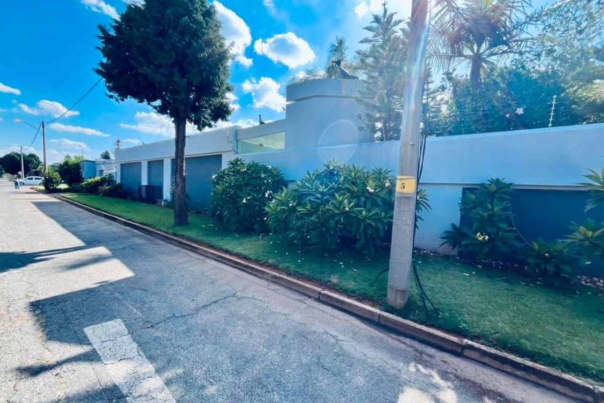 Street view of the property showing the boundary wall, electric fencing, and landscaped garden area along the paved verge.